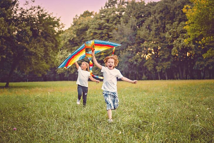 Deux enfants courent dans un champ en faisant voler un cerf-volant coloré sous le soleil d’été.