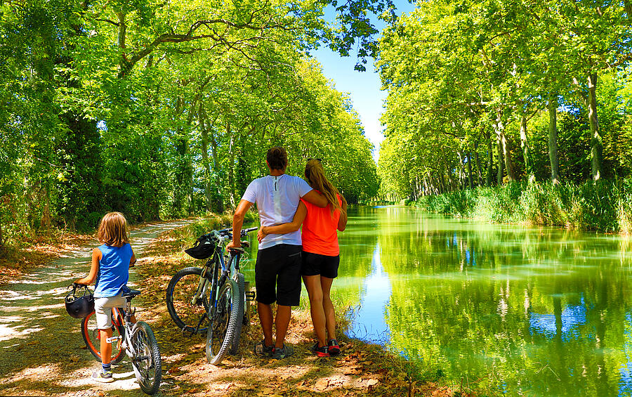 Famille en balade à vélo sur un chemin ombragé le long des abords du canal du Midi, en pleine nature.