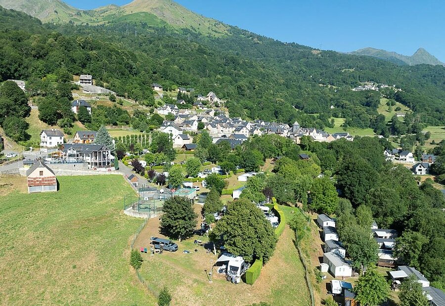 Vue aérienne d’un camping dans les Hautes-Pyrénées, proche d’un village de montagne typique, au cœur de la nature d’Occitanie.