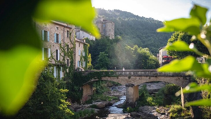 Vue sur le pont de Largentière, maisons en pierre et tour médiévale, entourés de verdure au bord de la rivière.