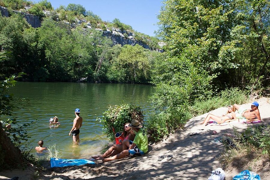 Familles profitant d’une baignade et se relaxant sur une plage ombragée au bord de la rivière, près des gorges de l’Ardèche.