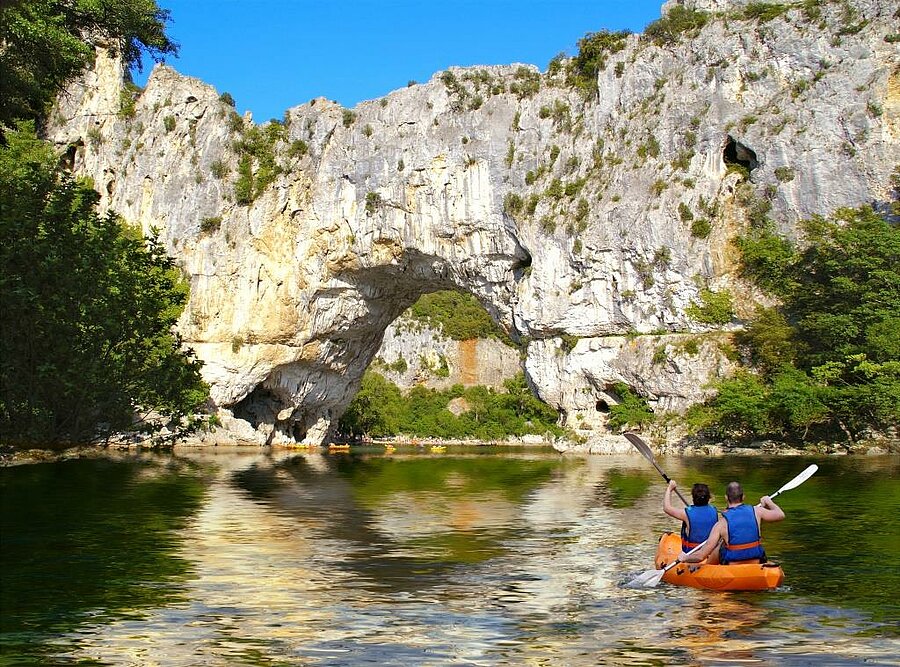 Canoë sous le Pont d’Arc, arche naturelle emblématique des gorges de l’Ardèche, une région à découvrir lors de vacances en camping.