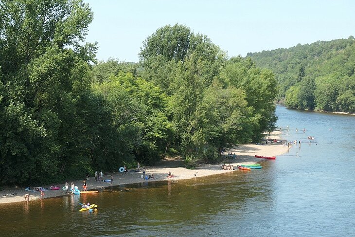 Plage au bord de la Vézère près du Bugue, avec baigneurs et canoës pour une sortie nature en Dordogne.