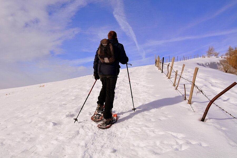 Un randonneur en raquettes progresse sur un sentier enneigé sous un ciel bleu, dans un cadre naturel préservé. Profitez d’un séjour en camping caravaneige pour vivre des vacances hivernales inoubliables avec Sites et Paysages.