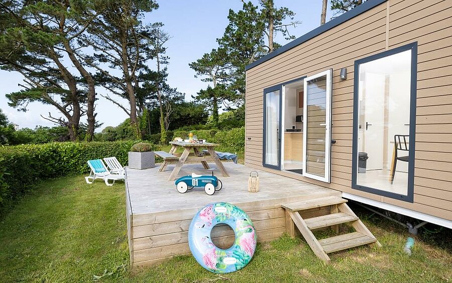 Mobil-home avec terrasse en bois, transats et coin repas dans un camping en Bretagne, idéal pour les familles