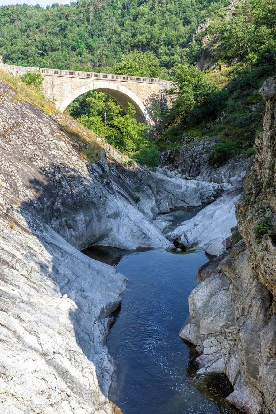 Un pont pittoresque enjambant les gorges de l’Ardèche, entouré de formations rocheuses et d’une nature verdoyante, parfait pour des vacances en camping en Ardèche. 