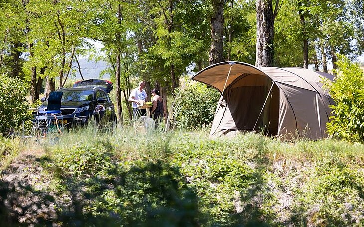 Couple installant sa tente à l’ombre des arbres, moment complice et serein d’un séjour Early Booking en pleine nature.