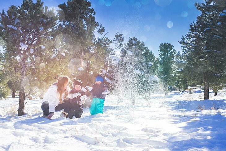 Famille jouant dans la neige au soleil, rires et complicité pendant les vacances d’hiver.