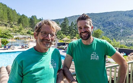 Deux propriétaires de campings Sites et Paysages posent avec le sourire, illustrant la satisfaction et la fierté d'appartenir à un réseau qui valorise le professionnalisme, la convivialité, le partage et l'accompagnement. Ils témoignent des valeurs humaines et de la cohésion qui font la force de Sites et Paysages, un réseau unique où l'authenticité et le respect de la nature sont au cœur de la promesse depuis 1982.