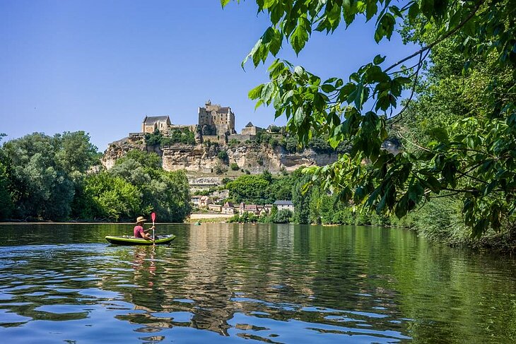Canoë sur la Dordogne avec un château perché en arrière-plan, activité nature idéale pour explorer la vallée en plein air.