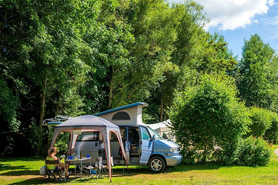 Camping van installé sur un emplacement van spacieux et ombragé, avec coin repas extérieur au cœur d’un cadre naturel verdoyant.