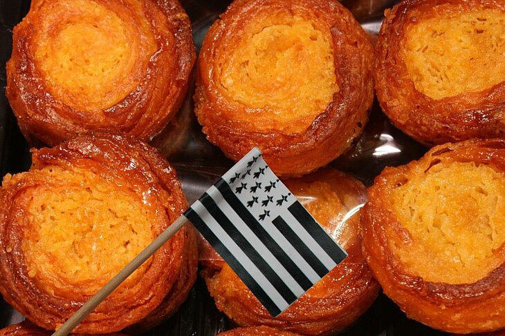 Kouign-amann doré, spécialité bretonne au beurre avec drapeau breton, emblème gourmand du Finistère Tourisme.