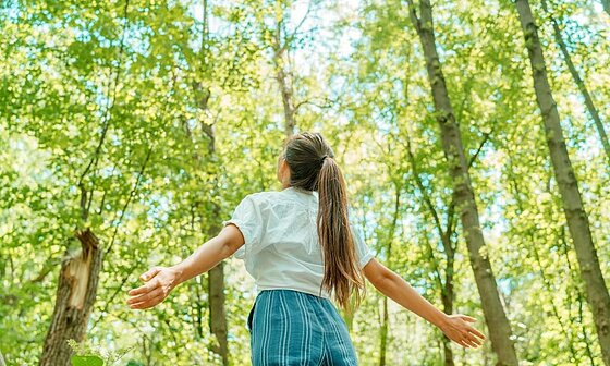Jeune fille les bras ouverts en pleine forêt, symbole de reconnexion à la nature et de tourisme durable avec Sites et Paysages.