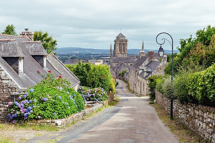 Rue pavée du village de Locronan dans le Finistère avec maisons en pierre et église, escale hors du temps du Finistère Tourisme.