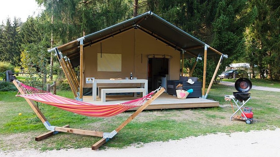 Tente équipée avec terrasse et hamac dans un cadre fleuri, idéale pour un séjour nature en toute sérénité.