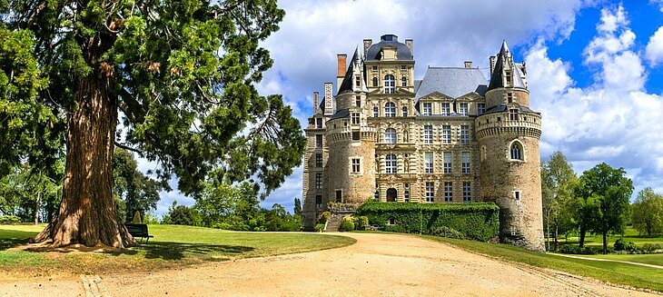 Le château de Brissac et son parc paysager en Anjou Façade du château de Brissac avec ses tours et ses hautes fenêtres, entourée d'un parc arboré dans le Maine-et-Loire.