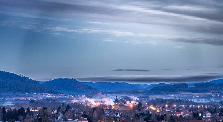 Vue du village de Corcieux au crépuscule, entouré de collines vosgiennes, illustrant le tourisme entre nature et patrimoine.