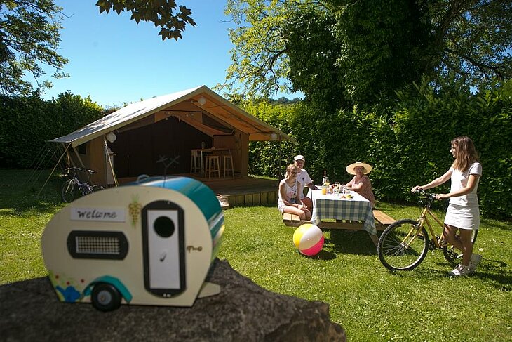 Vacances en famille dans un camping nature Sites et Paysages Famille devant une tente lodge dans un camping nature Sites et Paysages avec vélos et repas en plein air.