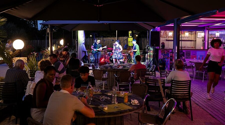 Soirée animée en camping avec concert en plein air, familles et amis réunis autour des tables dans une ambiance chaleureuse.