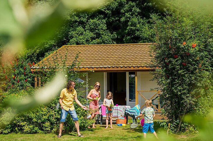 Famille jouant devant un chalet en bois au camping Au Clos de la Chaume à Corcieux, parfait pour un séjour nature et convivial dans les Vosges.