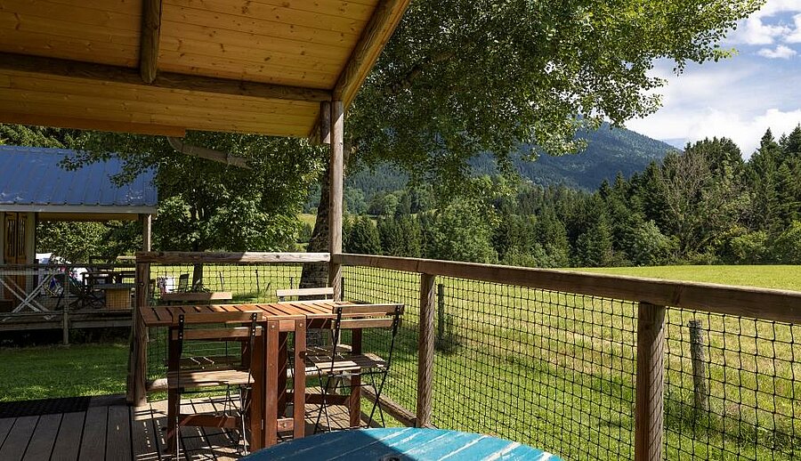 Terrasse couverte en bois dans un camping en Isère, face aux montagnes, au cœur d’un cadre naturel paisible