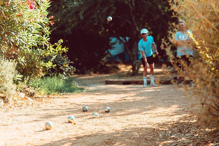 Partie de pétanque conviviale en plein air sous le soleil dans un camping en Corse, entourée de végétation méditerranéenne, idéale pour des vacances en famille ou entre amis.