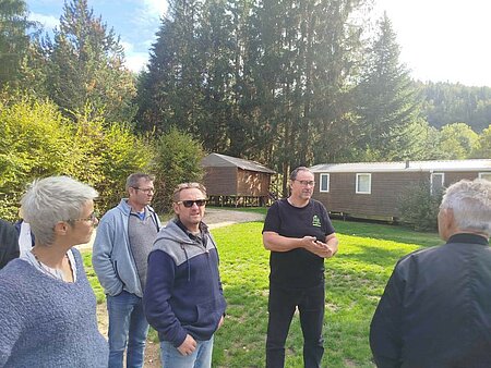 Plusieurs adhérents du réseau Sites et Paysages échangent lors d'une visite de camping, au milieu des hébergements et dans un environnement boisé.