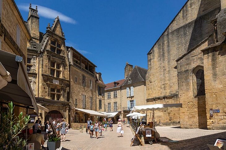 Place animée de Sarlat-la-Canéda avec ruelles pavées et façades en pierre, village de caractère incontournable en Dordogne.