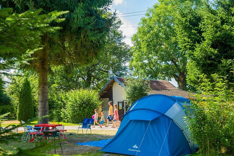 Séjour en camping au cœur du Grand Est, avec une tente installée dans un cadre verdoyant. Une famille profite d’un moment convivial sous les arbres, près des installations du camping.