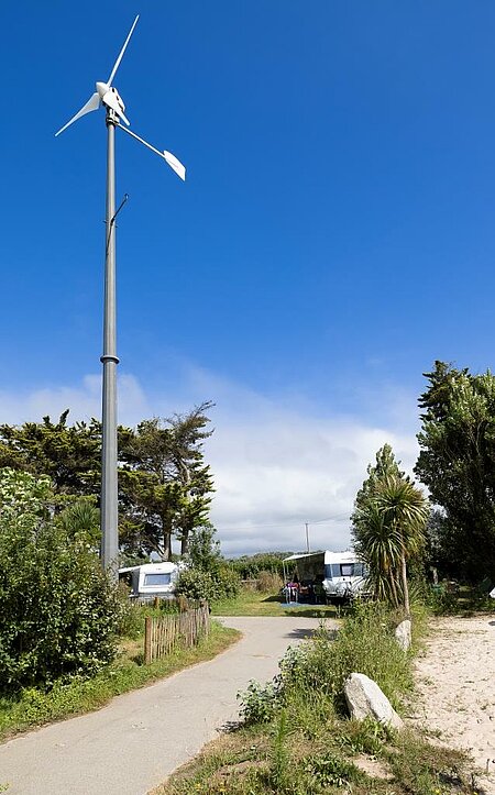 Éolienne dans un camping nature, illustrant l’engagement collectif de Sites et Paysages pour un tourisme durable et des énergies renouvelables.