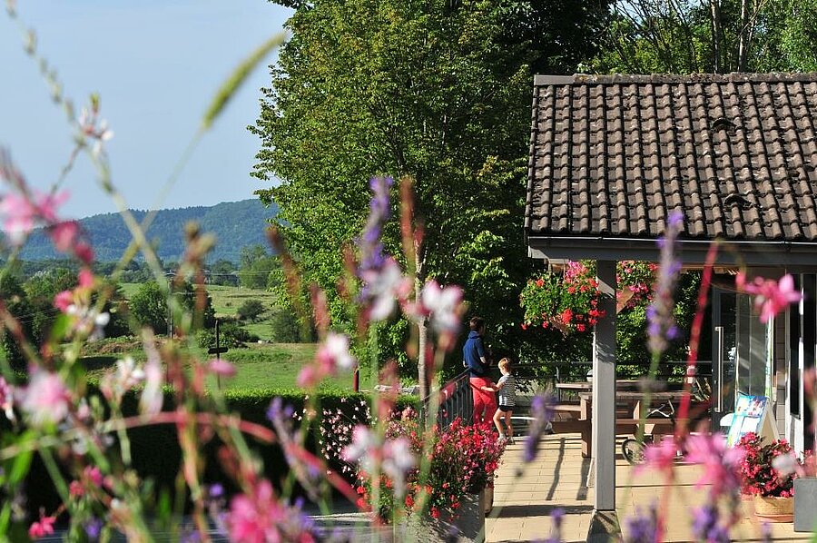 Famille sur la terrasse fleurie d’un hébergement de camping avec vue sur la nature en Bourgogne-Franche-Comté.