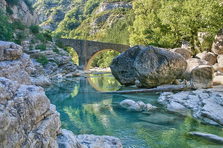 Paysage naturel des gorges de la Méouge près de Sisteron, avec son pont de pierre historique et ses eaux turquoise, un lieu idéal pour des activités en pleine nature comme la randonnée et la baignade.