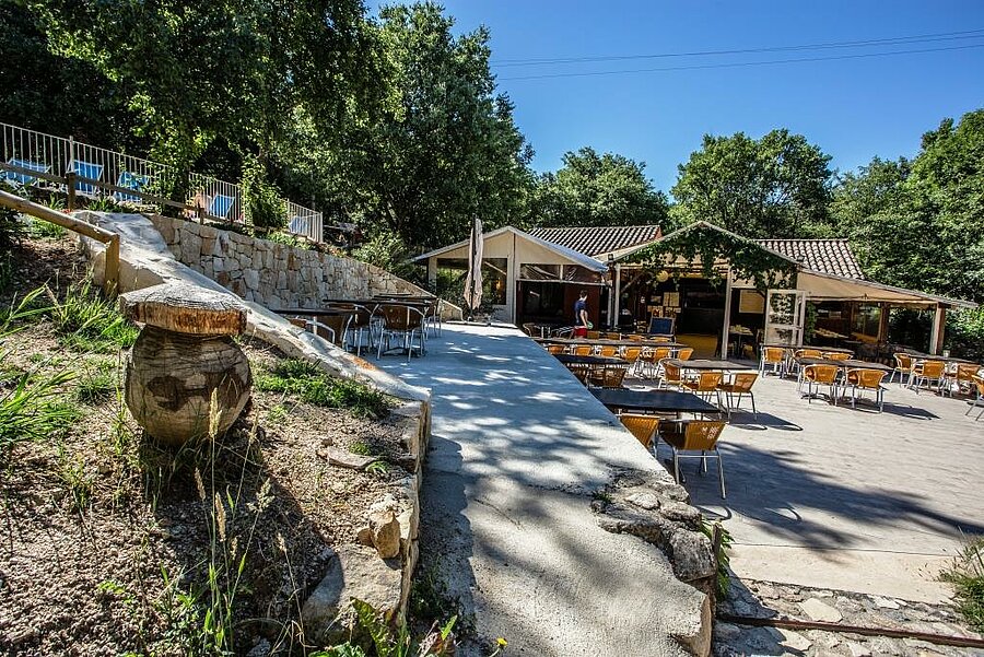 Terrasse ombragée du restaurant dans un camping à proximité de Vallon Pont d’Arc, idéale pour des vacances conviviales en pleine nature.