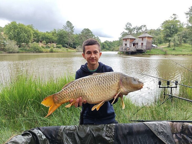Jeune pêcheur tenant une carpe au Domaine de l’Étang de Bazange à Monfaucon, une activité nature pour petits et grands en Dordogne.