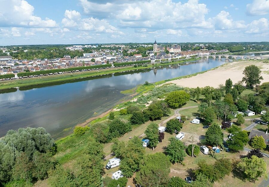 Vue aérienne d’un camping verdoyant en bord de Loire, près de la Sologne, face à la ville de Gien et son pont emblématique