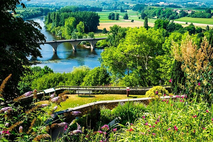 Vue sur Limeuil et la vallée, avec la Vézère, un pont de pierre et un jardin en hauteur en Dordogne.