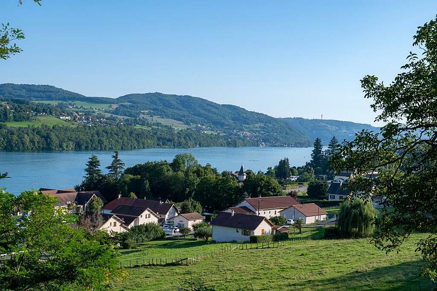 Vue panoramique du lac de Paladru en Isère, entouré de collines verdoyantes et de charmants villages, un cadre idéal pour des vacances en camping alliant nature et activités nautiques.