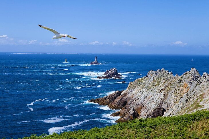 La Pointe du Raz en Bretagne Falaises escarpées de la Pointe du Raz en Bretagne, mer agitée et phare au large, site naturel spectaculaire à découvrir quand on se demande que faire en Bretagne.
