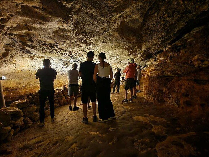 Groupe de visiteurs découvrant une galerie rocheuse éclairée dans la grotte de Bara-Bahau, au Bugue, en Dordogne.
