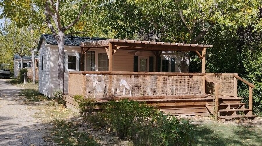 Mobil-home avec terrasse couverte en bois et salon de jardin, installé sous les arbres au Domaine de l’Écluse, près du Mont Ventoux.