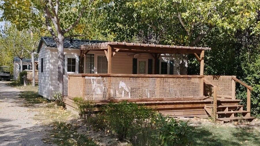 Mobil-home avec terrasse couverte en bois et salon de jardin, installé sous les arbres au Domaine de l’Écluse, près de Nyons.