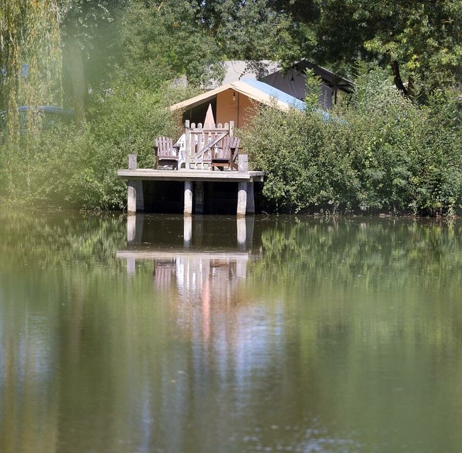 Tente lodge confortable avec terrasse en bois surplombant un étang, nichée en pleine nature, idéale pour un séjour insolite près des Châteaux de la Loire.