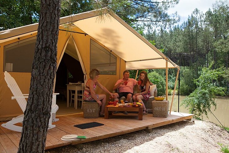 Famille profitant d’un moment de détente devant une tente safari au Domaine de l’Étang de Bazange à Monfaucon, une expérience glamping mémorable en Dordogne.