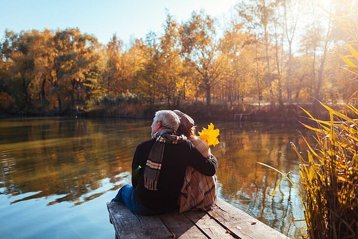 Profiter d’un court séjour à deux en automne Couple assis au bord d’un lac profitant d’un moment calme au soleil en automne.