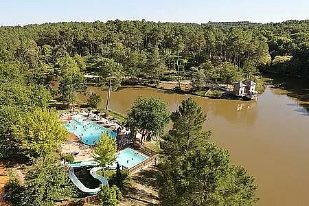 Vue aérienne du camping Domaine de l'Etang de Bazange, avec piscine et toboggan au bord d’un lac, au cœur d’une forêt