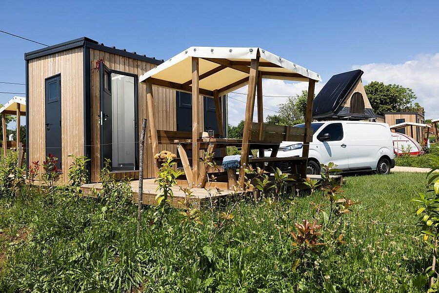 Emplacement van tout confort avec sanitaires privés, mobilier de jardin et van aménagé, dans un camping nature en France.