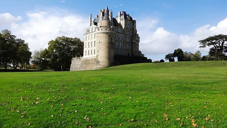 Le château de Brissac, joyau du patrimoine historique et culturel de Brissac Loire Aubance, entouré de verdure sous un ciel dégagé.