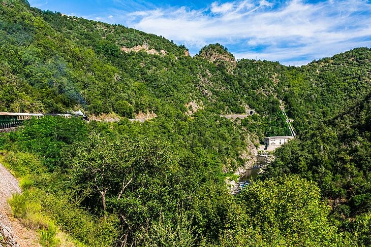 Train de l’Ardèche serpentant à flanc de montagne dans un paysage verdoyant près de Tournon-Saint-Jean, une expérience incontournable autour d’Eclassan pour les amateurs de nature et de patrimoine ferroviaire.