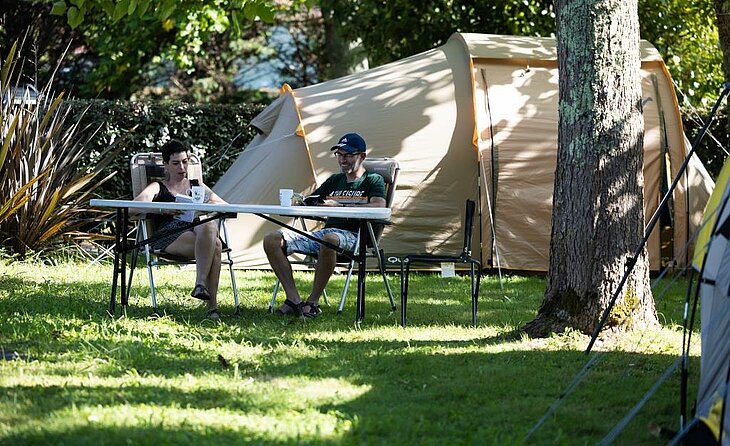 Couple devant une tente sur un emplacement verdoyant, illustration d’une offre Early Booking simple et transparente.