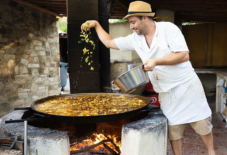 Julien préparant sa célèbre paëlla au feu de bois au restaurant du camping La Pinède, moment convivial et emblématique du tourisme à Lézignan-Corbières, entre recettes de famille et produits du potager.